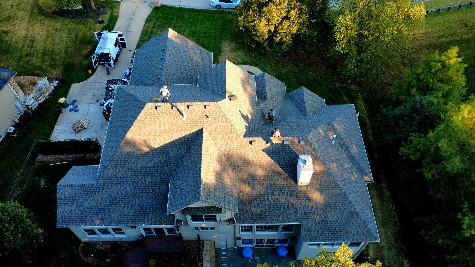 An aerial view of a house undergoing roof replacement, with construction workers on the gray shingled roof.
