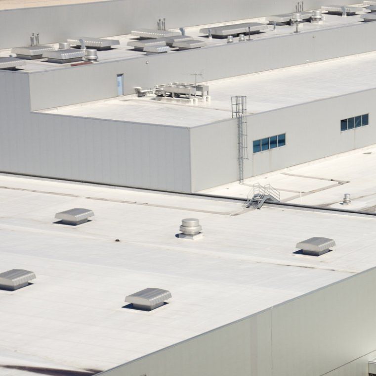 High-angle view of a flat, light-gray industrial building roof with multiple ventilation units and a metal ladder.