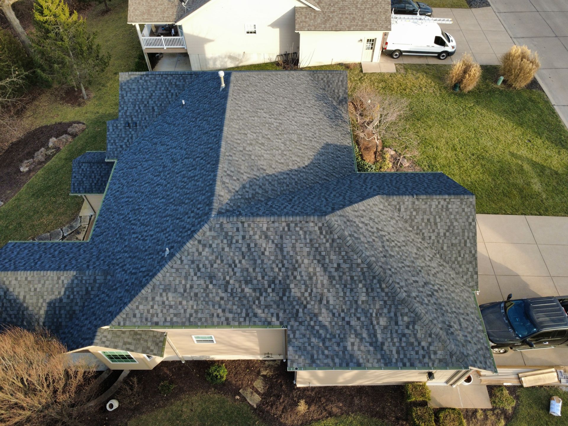 An aerial view of a residential house with a dual-toned gray and blue asphalt shingle roof, seen from above.