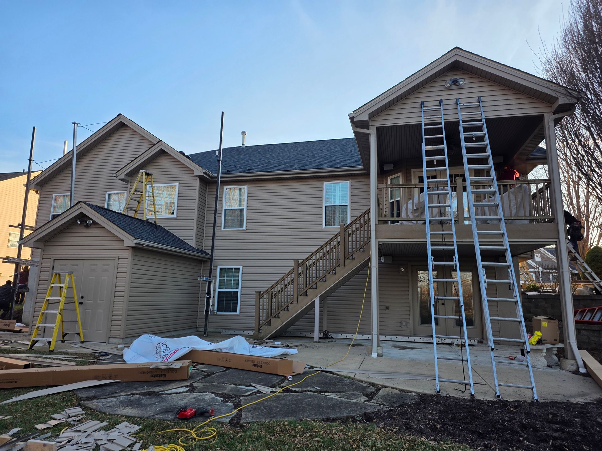 Two-story house under construction with ladders, scaffolding, and workers’ tools in the front yard