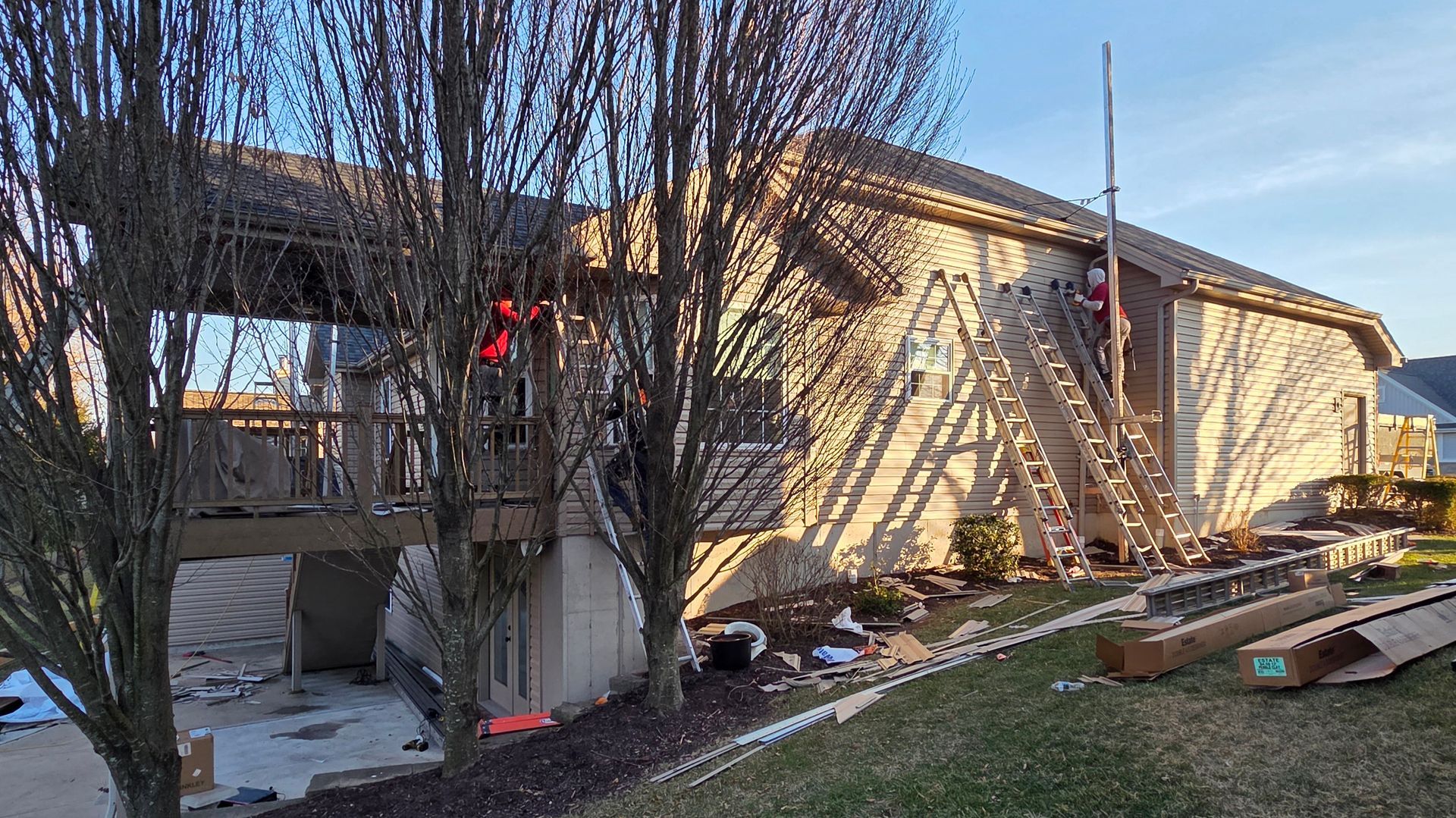 Damaged house exterior with a collapsed side porch, debris, and a ladder against the wall.