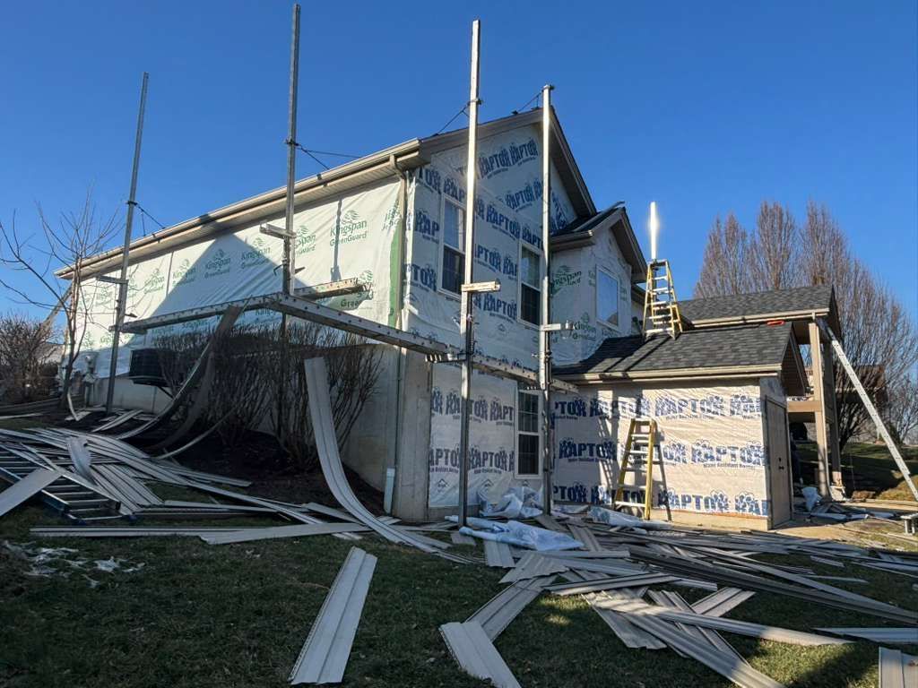 Damaged house with collapsed roof and debris scattered across the yard under a clear blue sky