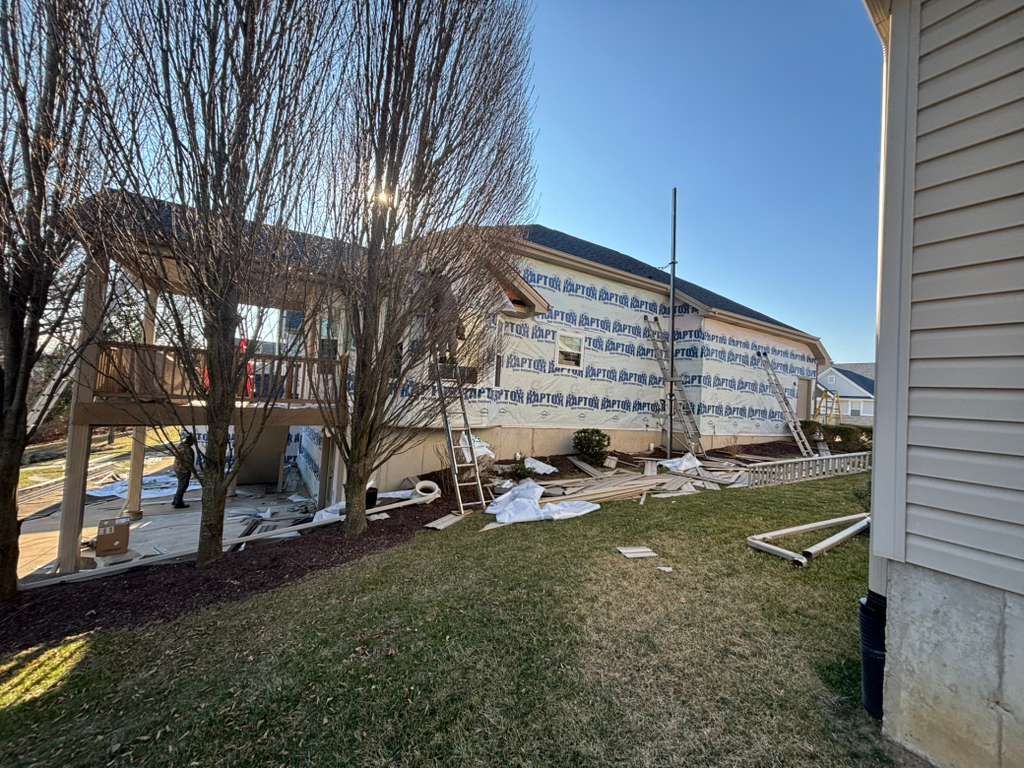 Damaged building exterior with torn siding, bare trees, and patchy snow on the ground
