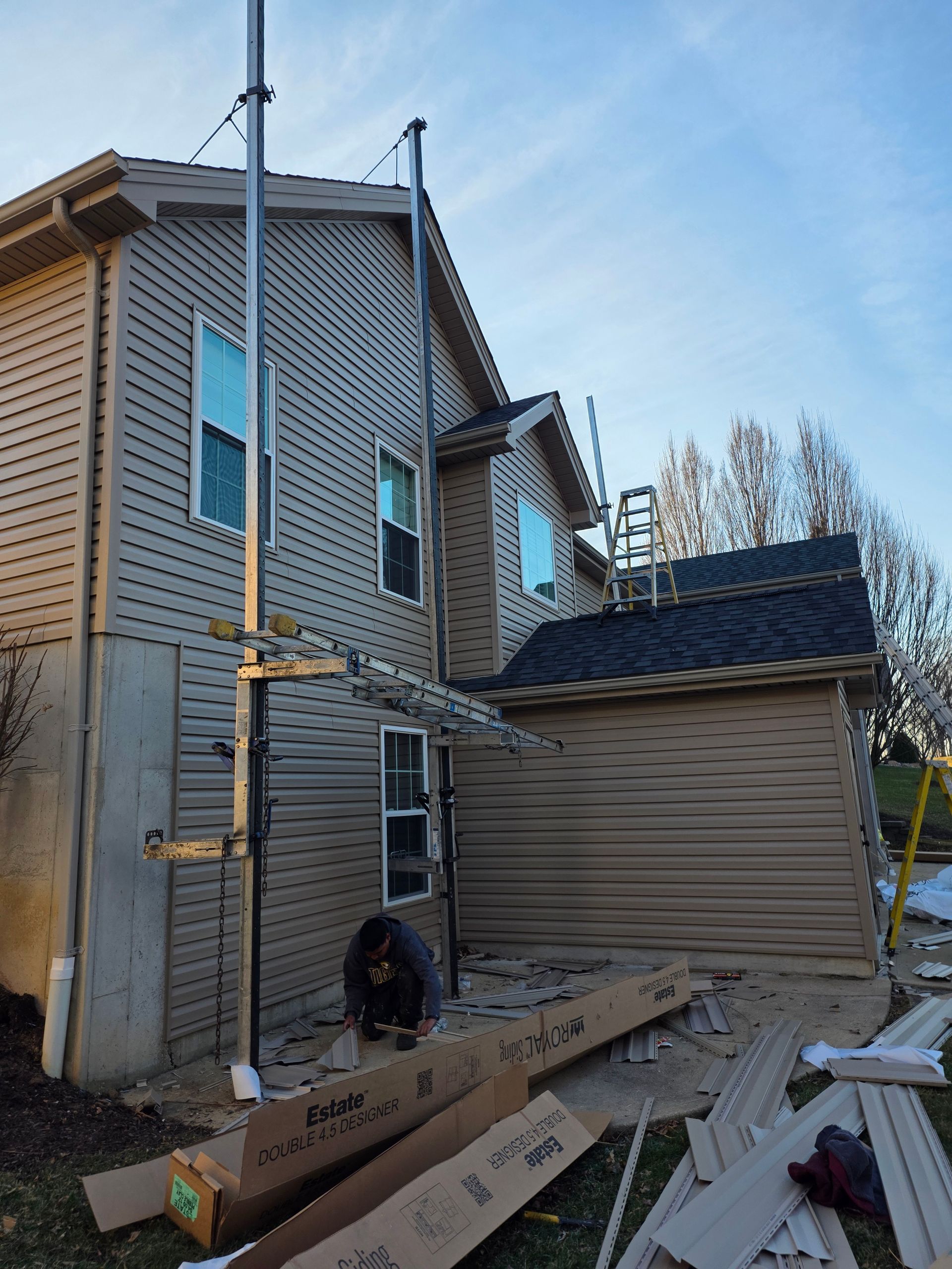 Exterior of a house under construction with scaffolding, siding, and scattered lumber in the yard