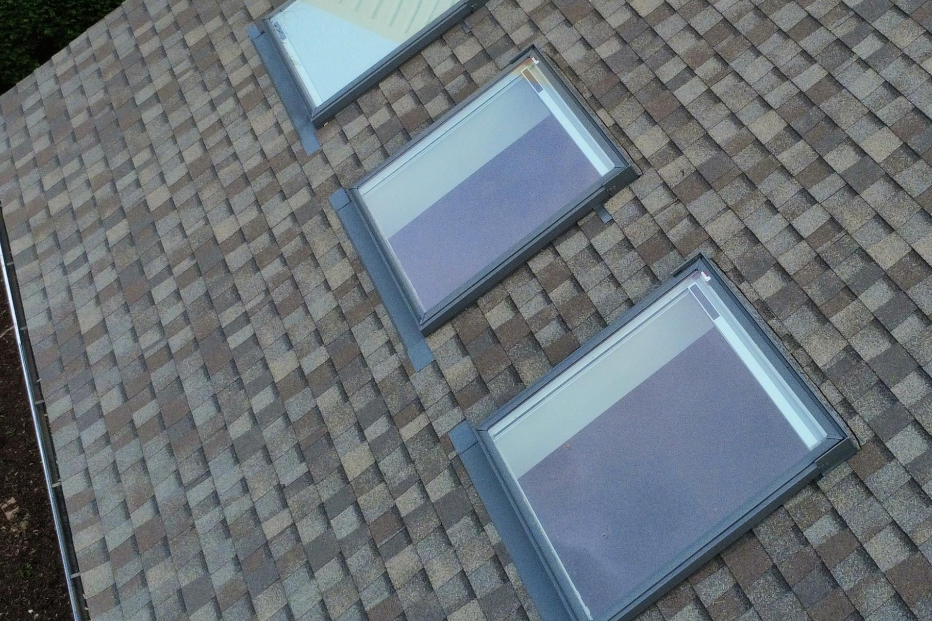Workers installing new multi-colored shingles on the roof of a grey, two-story house with a ladder leaning against it.