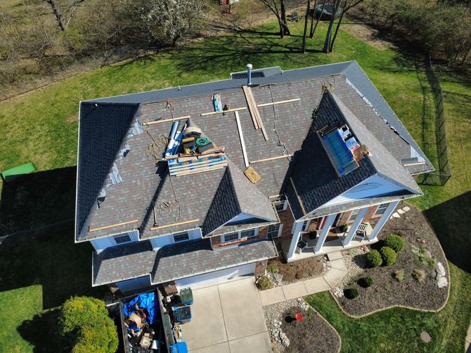 Aerial view of a house undergoing a roof replacement with shingles and scaffolding visible on the gray roof.