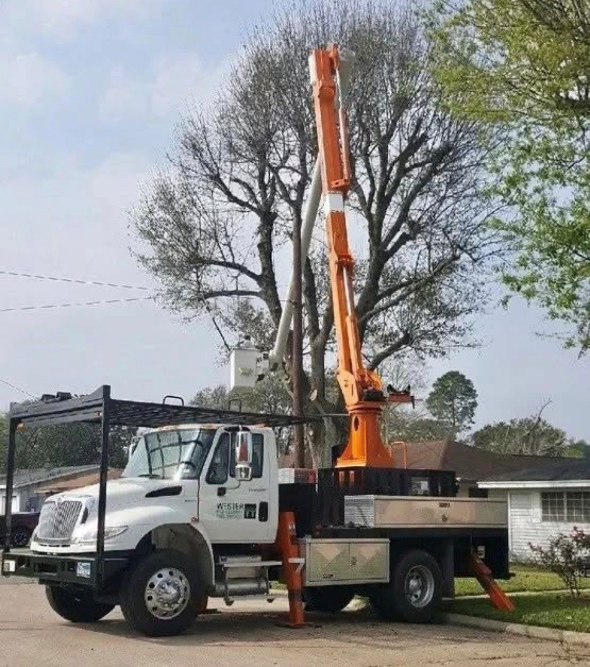 A truck with a crane attached to it is parked in front of a tree.