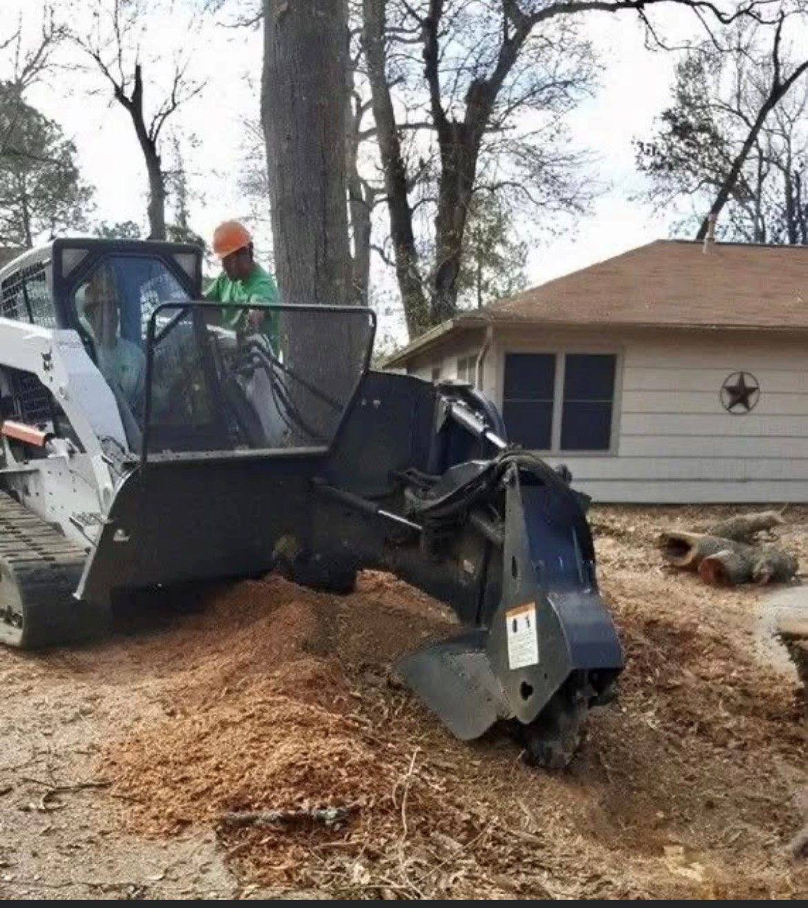 A man is working on a stump grinder in front of a house.