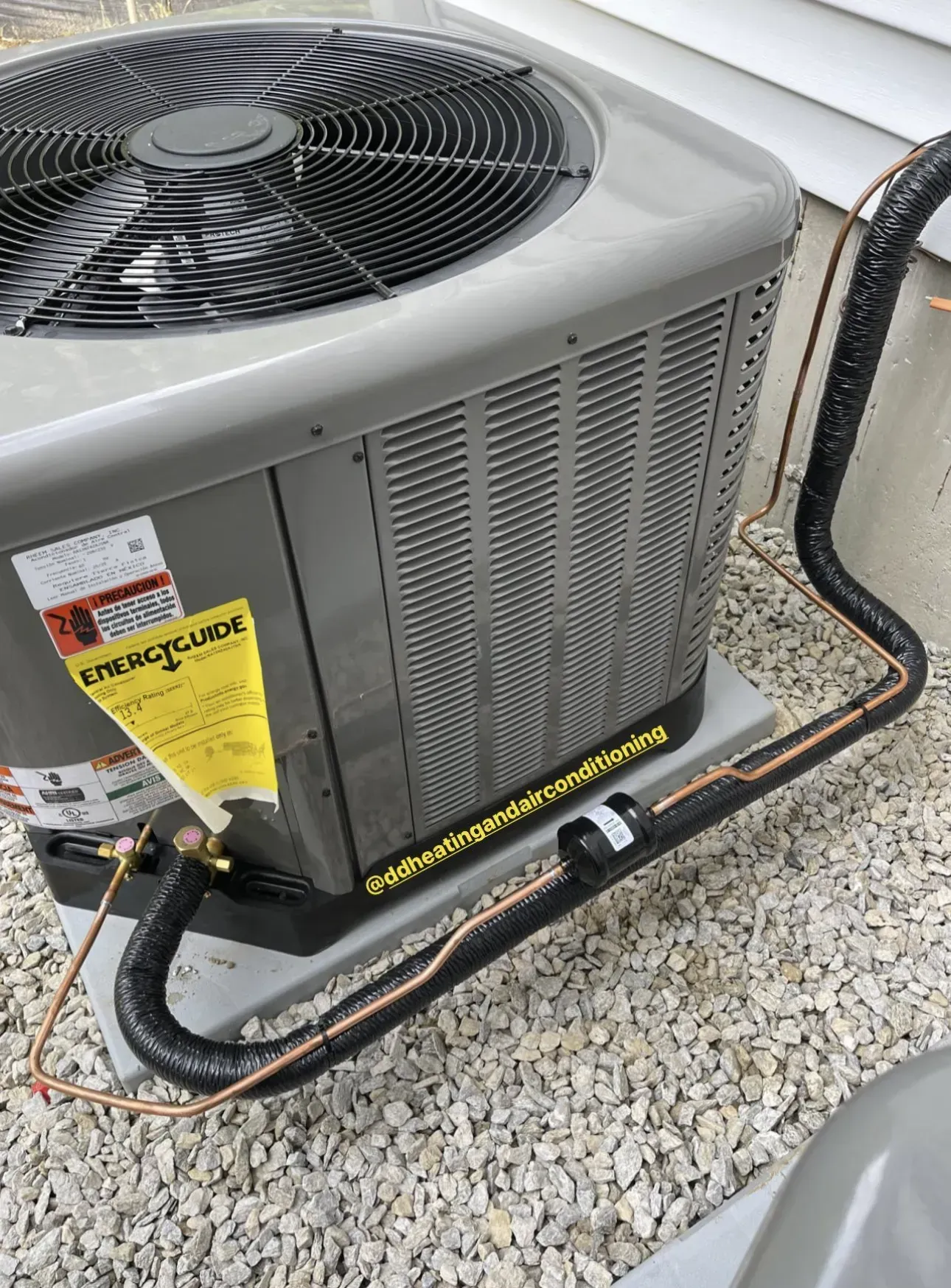 Outdoor HVAC condenser unit with black fan, gray metal sides, and yellow service tags on gravel.
