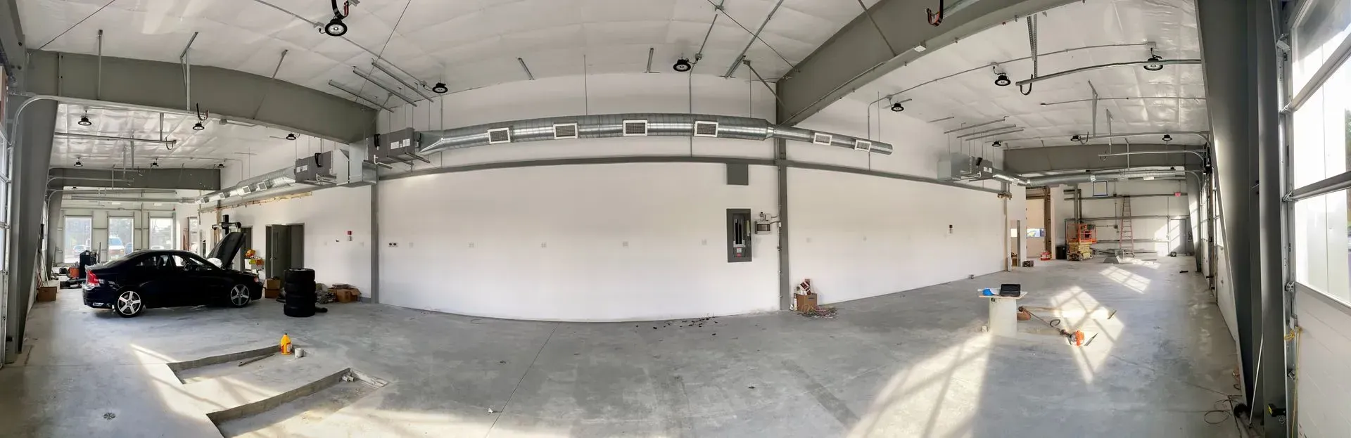 Empty industrial garage interior with white walls, concrete floor, and a black car parked on the left.