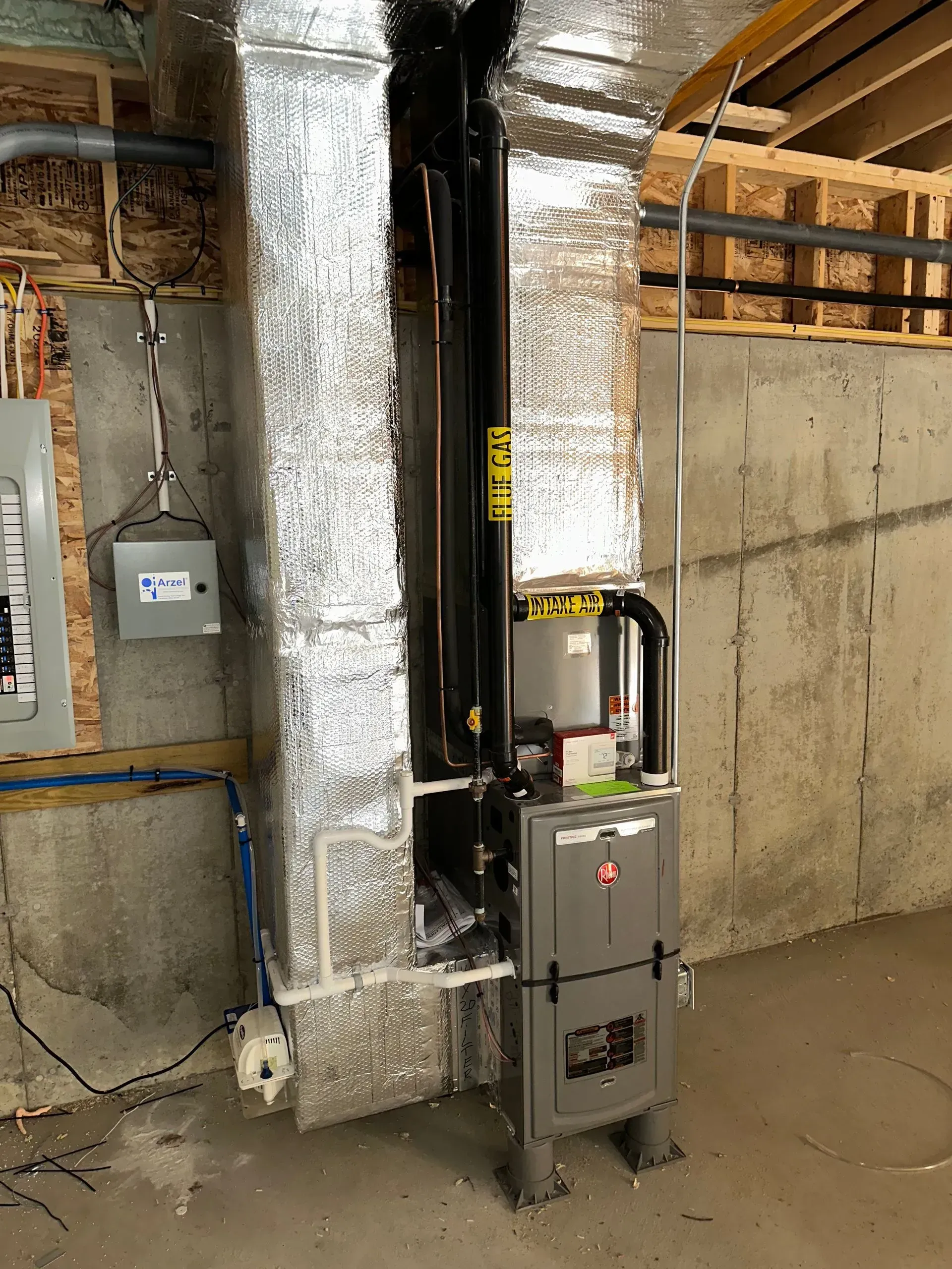 Basement utility room with insulated ductwork, pipes, and a gray HVAC/furnace unit near a concrete wall.