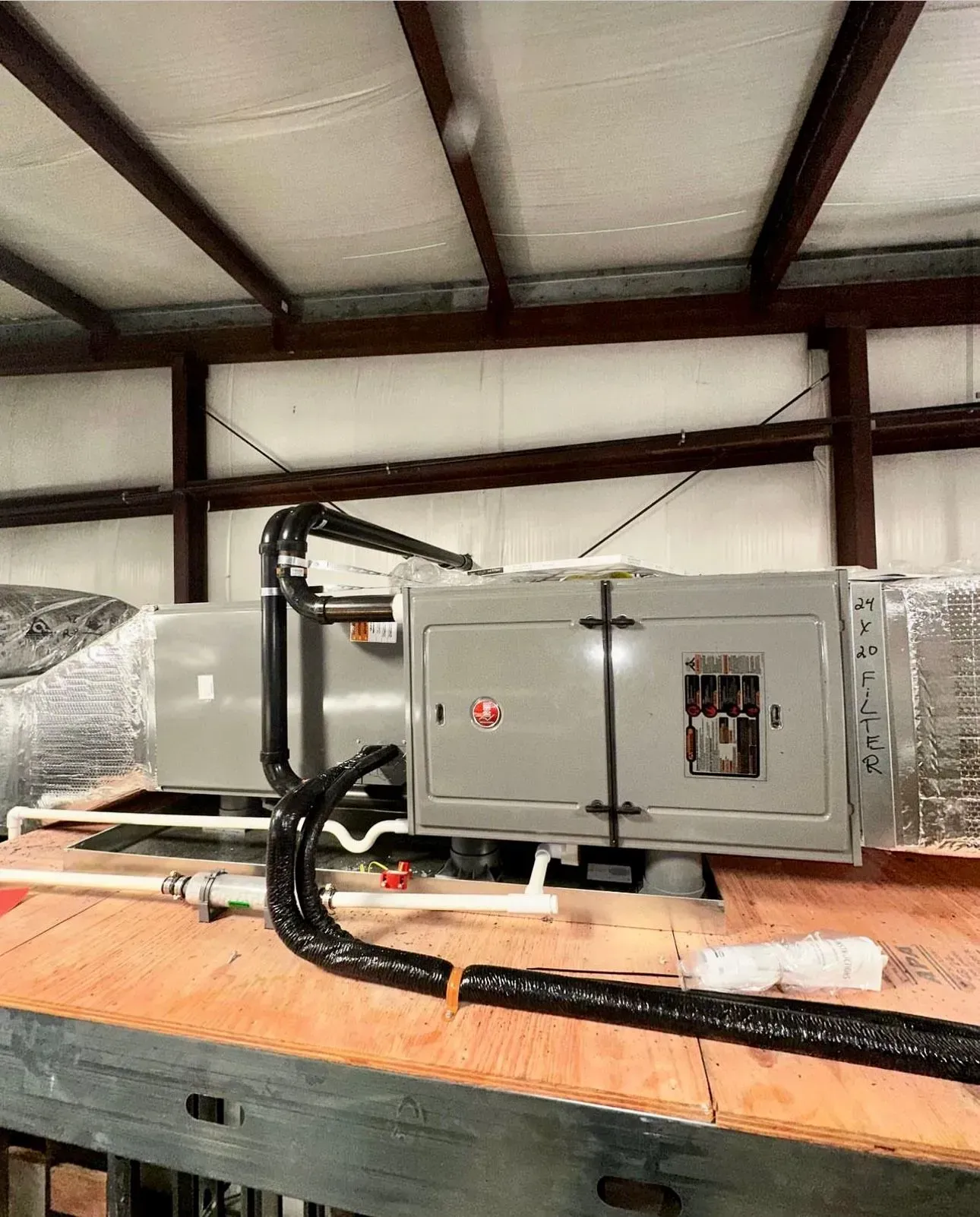 Industrial HVAC unit on a wooden pallet in a warehouse, wrapped in protective plastic.