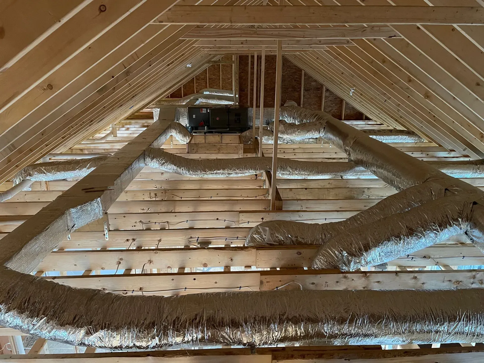Attic with exposed wooden rafters, insulation, and a small mechanical unit at the far end