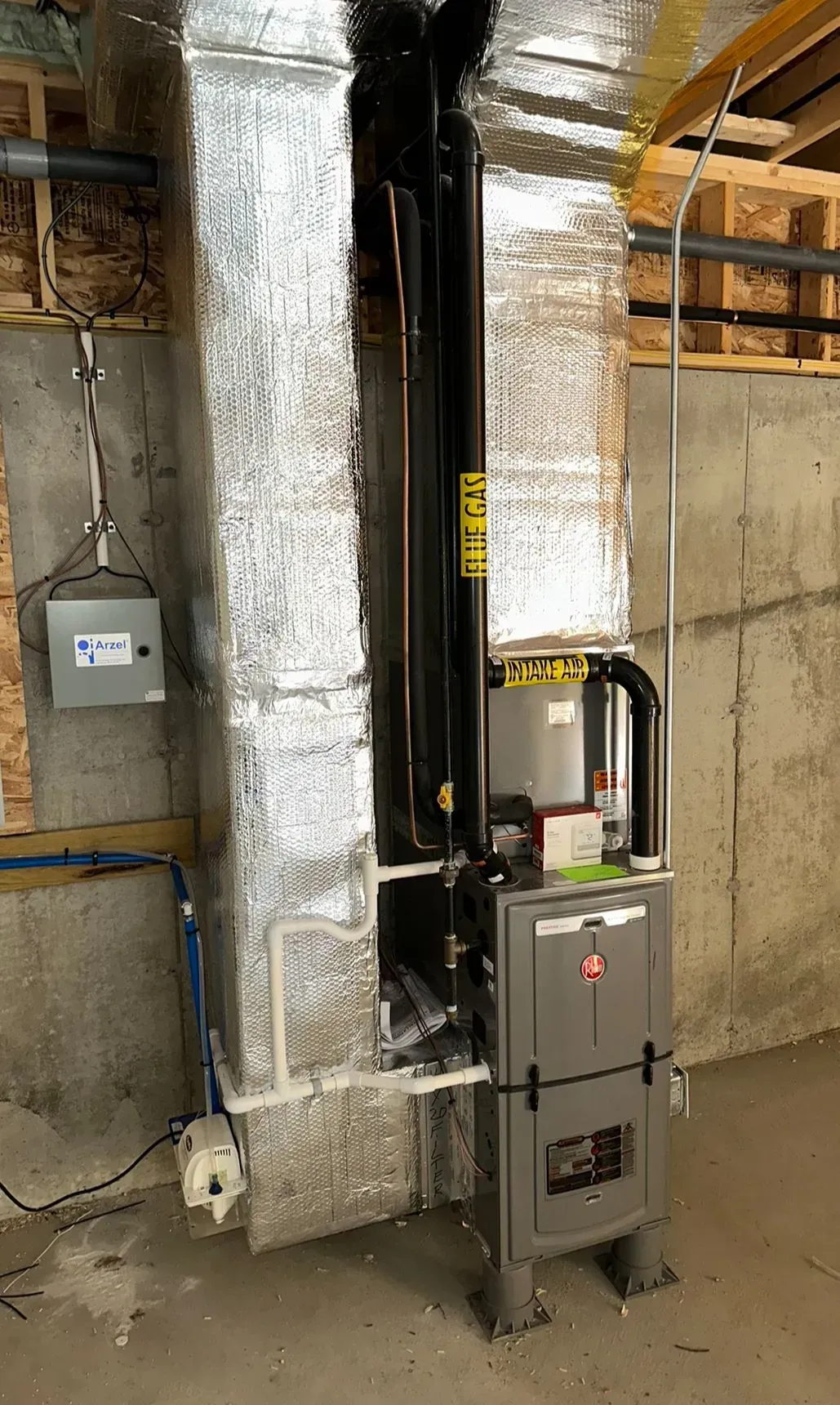 Industrial basement with insulated ductwork, a black pipe, and a gray utility cabinet against a concrete wall