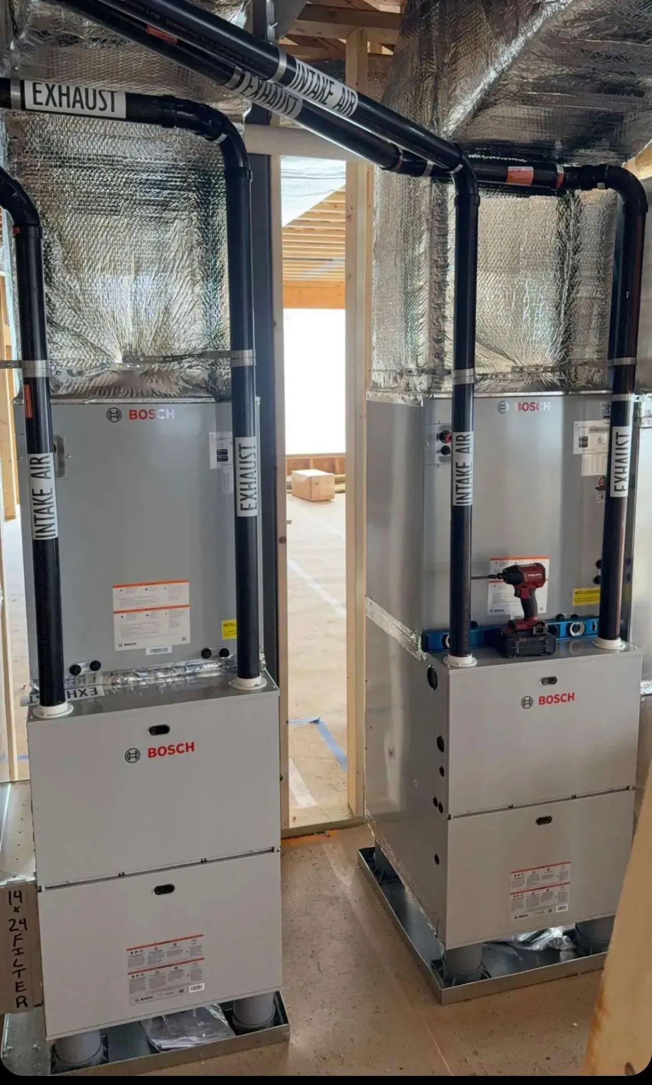 Two white HVAC units installed side by side in a utility room with insulated ductwork overhead