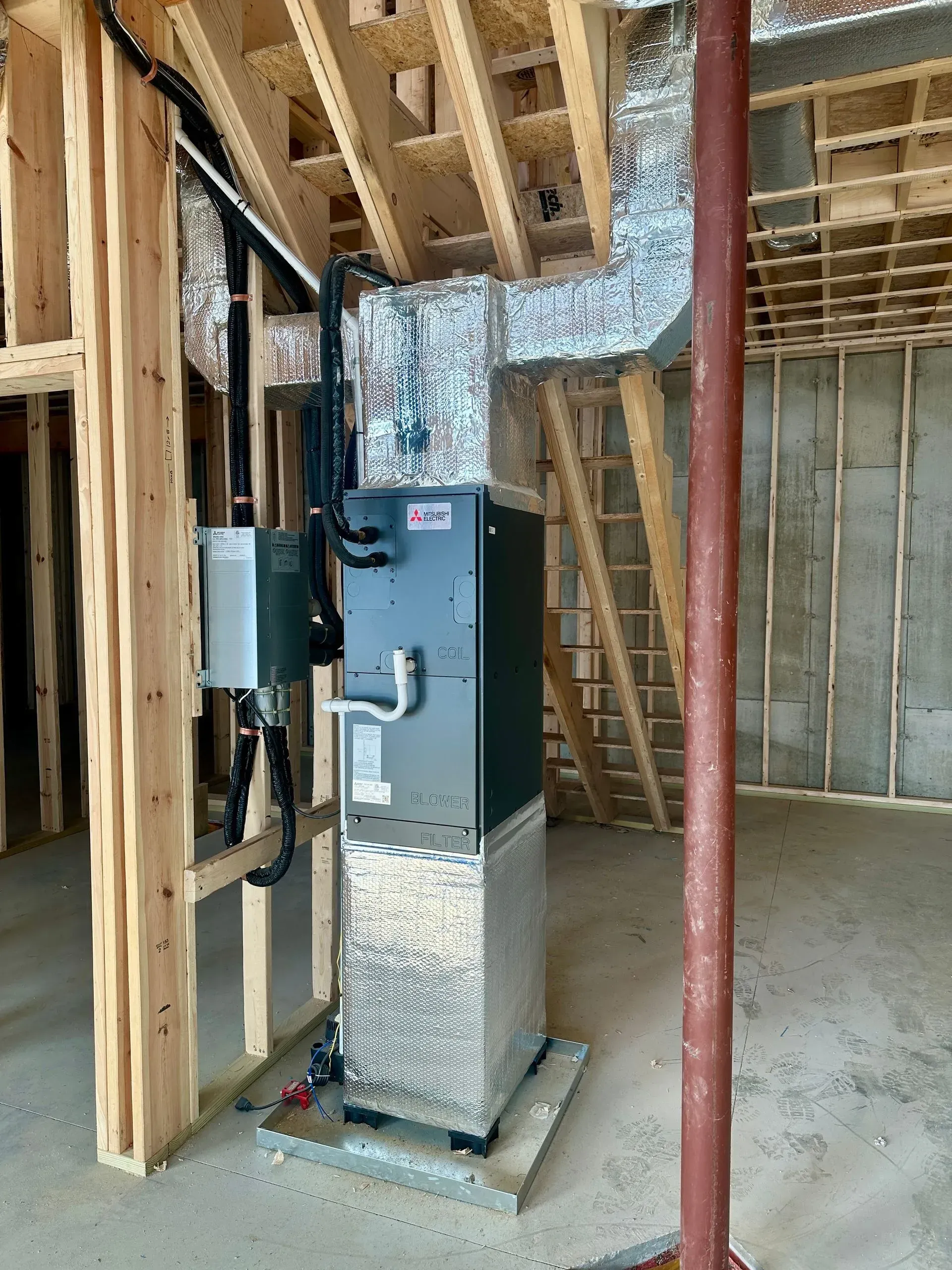 Furnace and water heater installed in an unfinished basement framed with exposed wood studs and ductwork