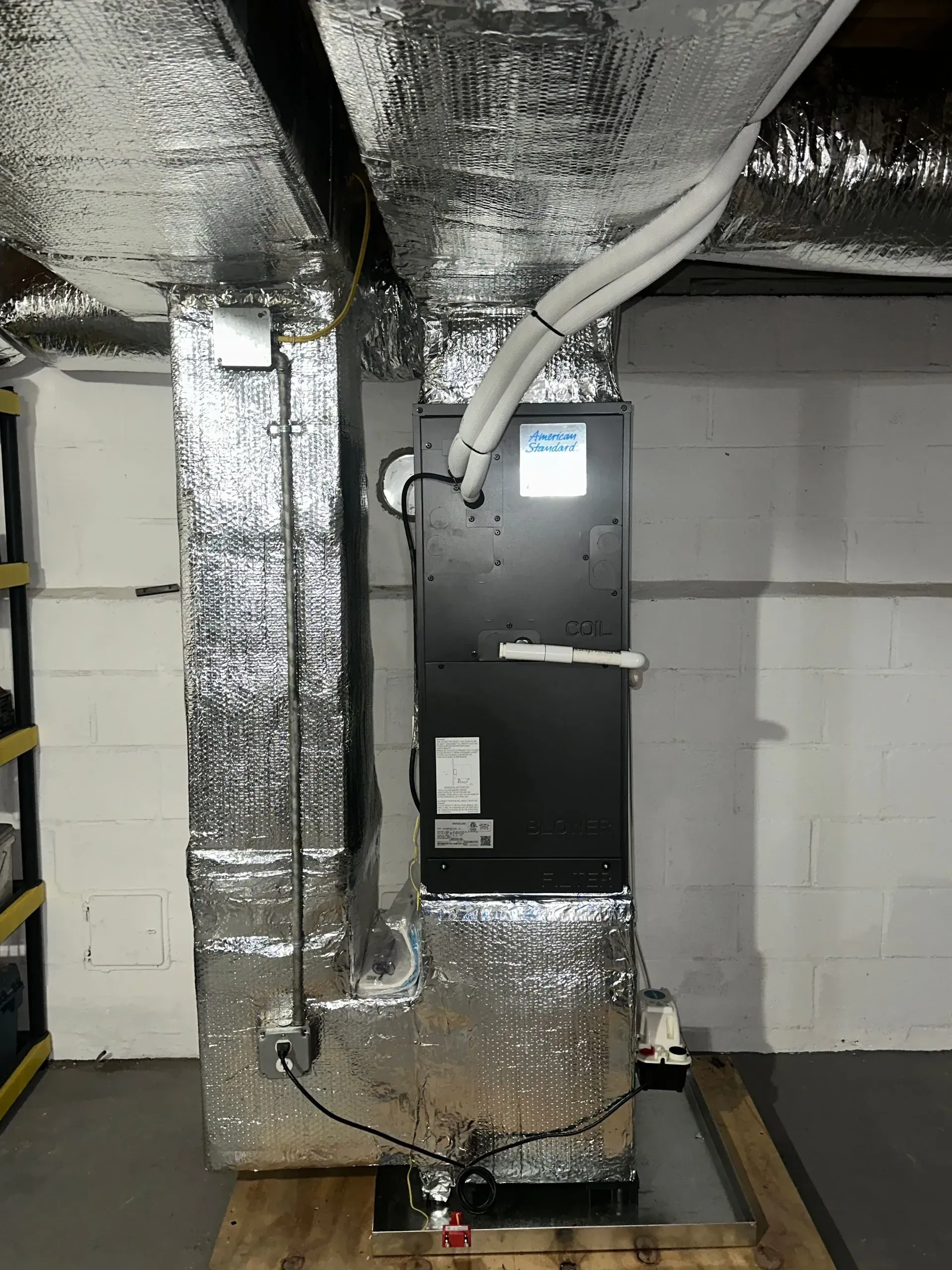 Insulated HVAC furnace in a utility room with silver ductwork and white cinderblock walls