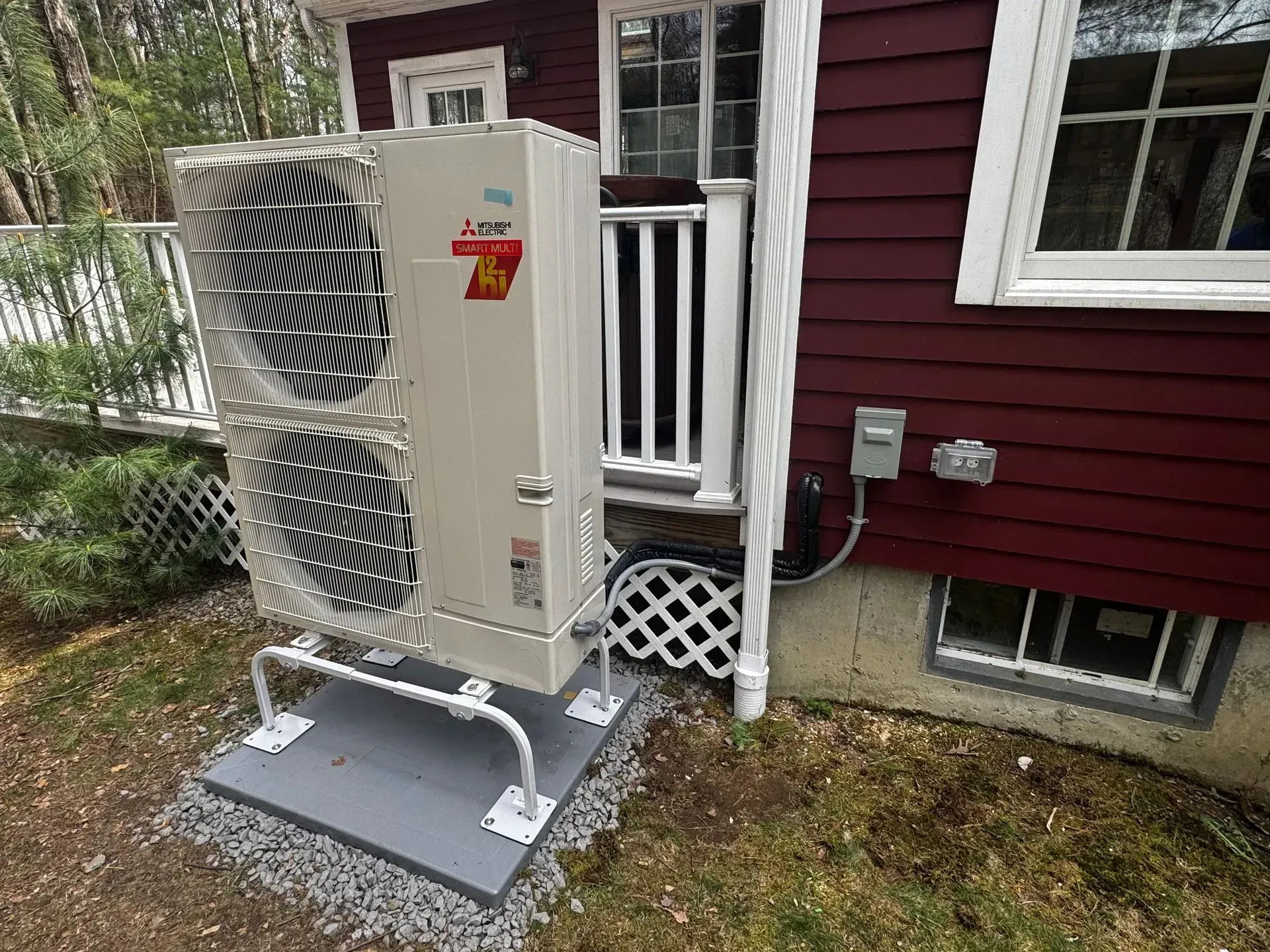 Outdoor HVAC unit on a raised platform beside a maroon house with a white railing.