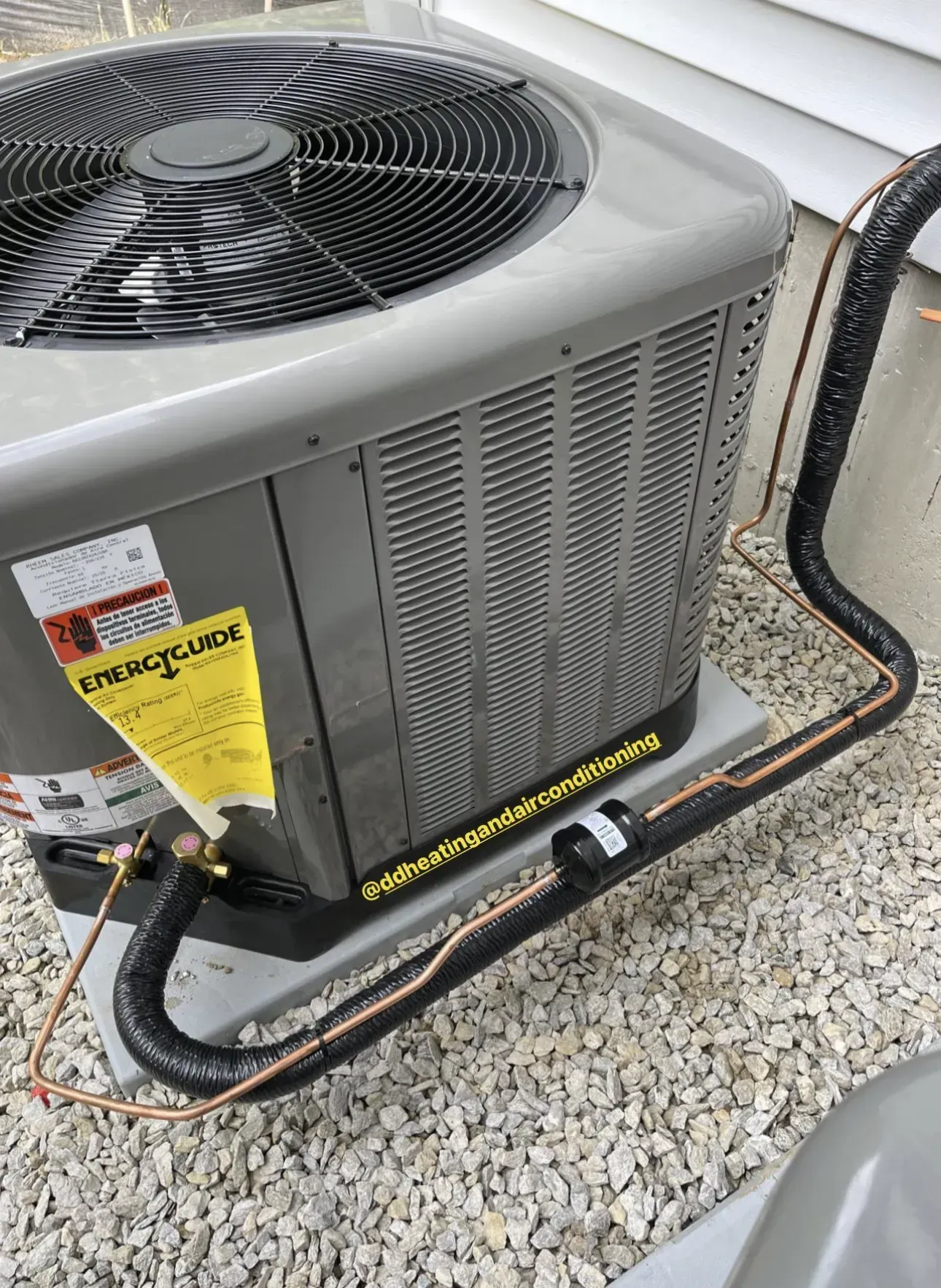 Outdoor HVAC condenser unit beside a house, with yellow repair tag and insulated refrigerant lines on gravel.