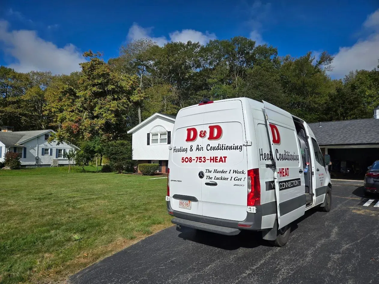 White D&D van parked in a suburban driveway beside a house and lawn under a blue sky.