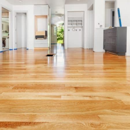 Polished wooden floor in an empty room with white walls, cabinets, and doorways, light streaming in.
