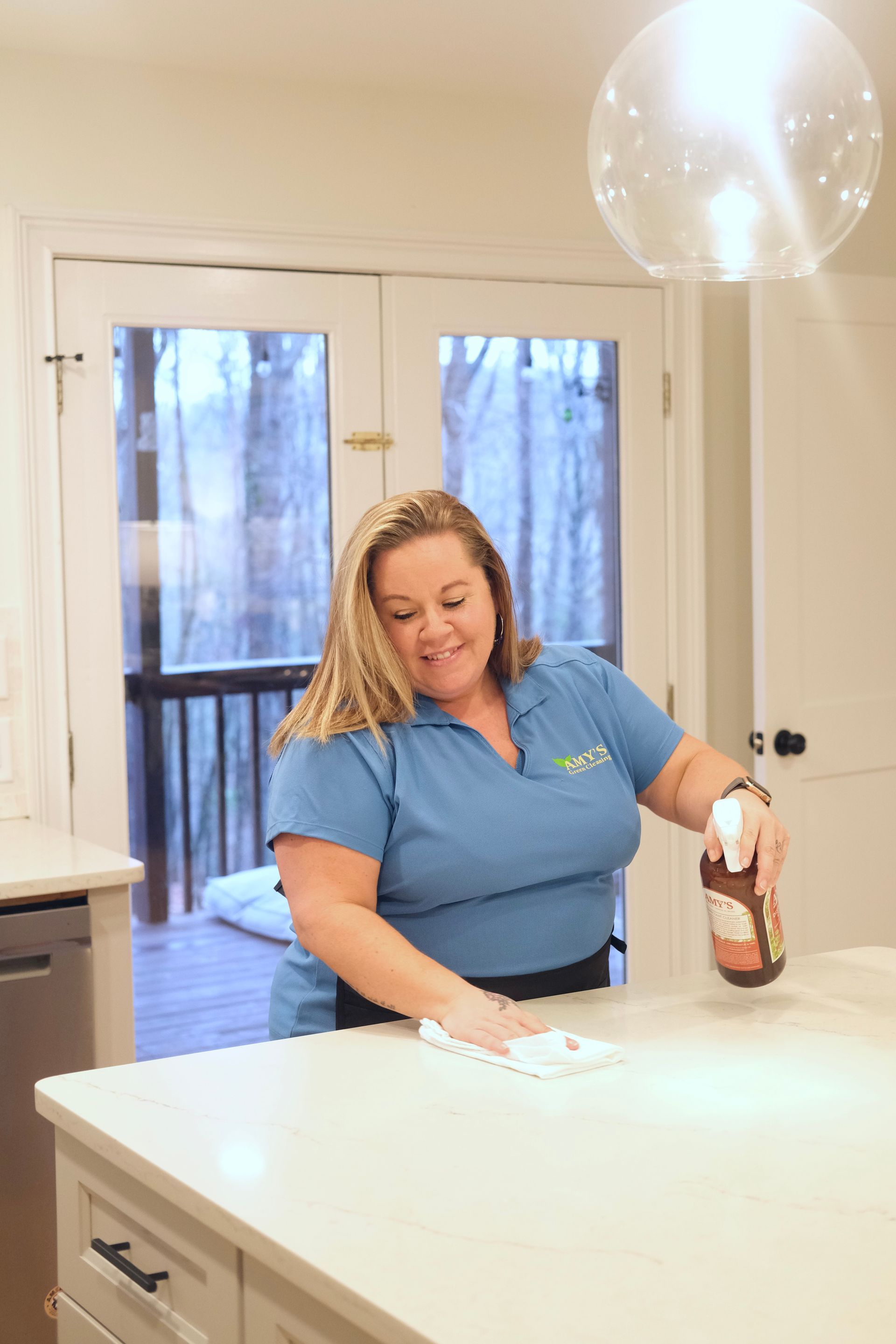 Woman in blue shirt cleaning a white kitchen counter with spray bottle and cloth.