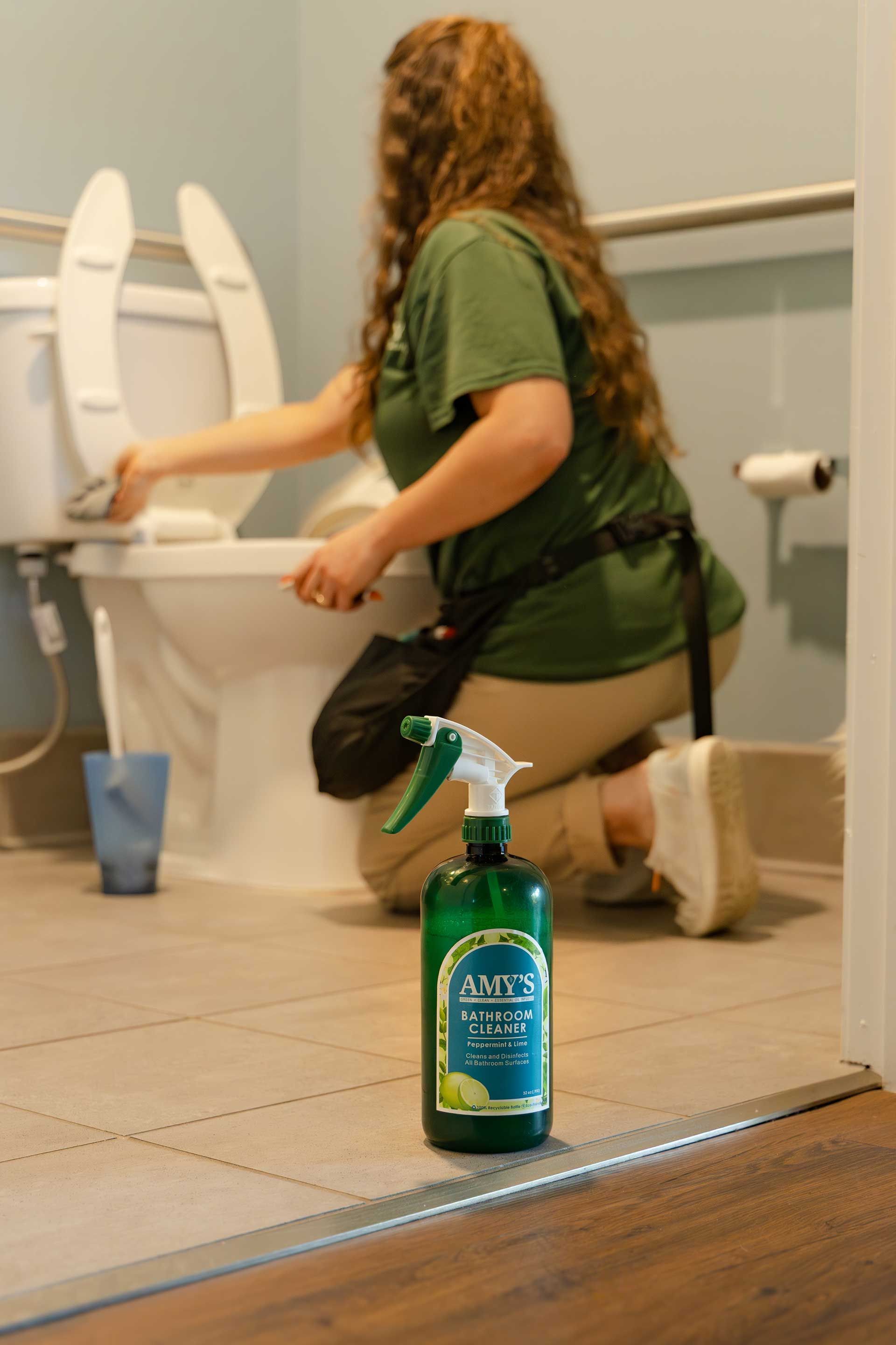 a person cleans a toilet in a bathroom, spray bottle in foreground