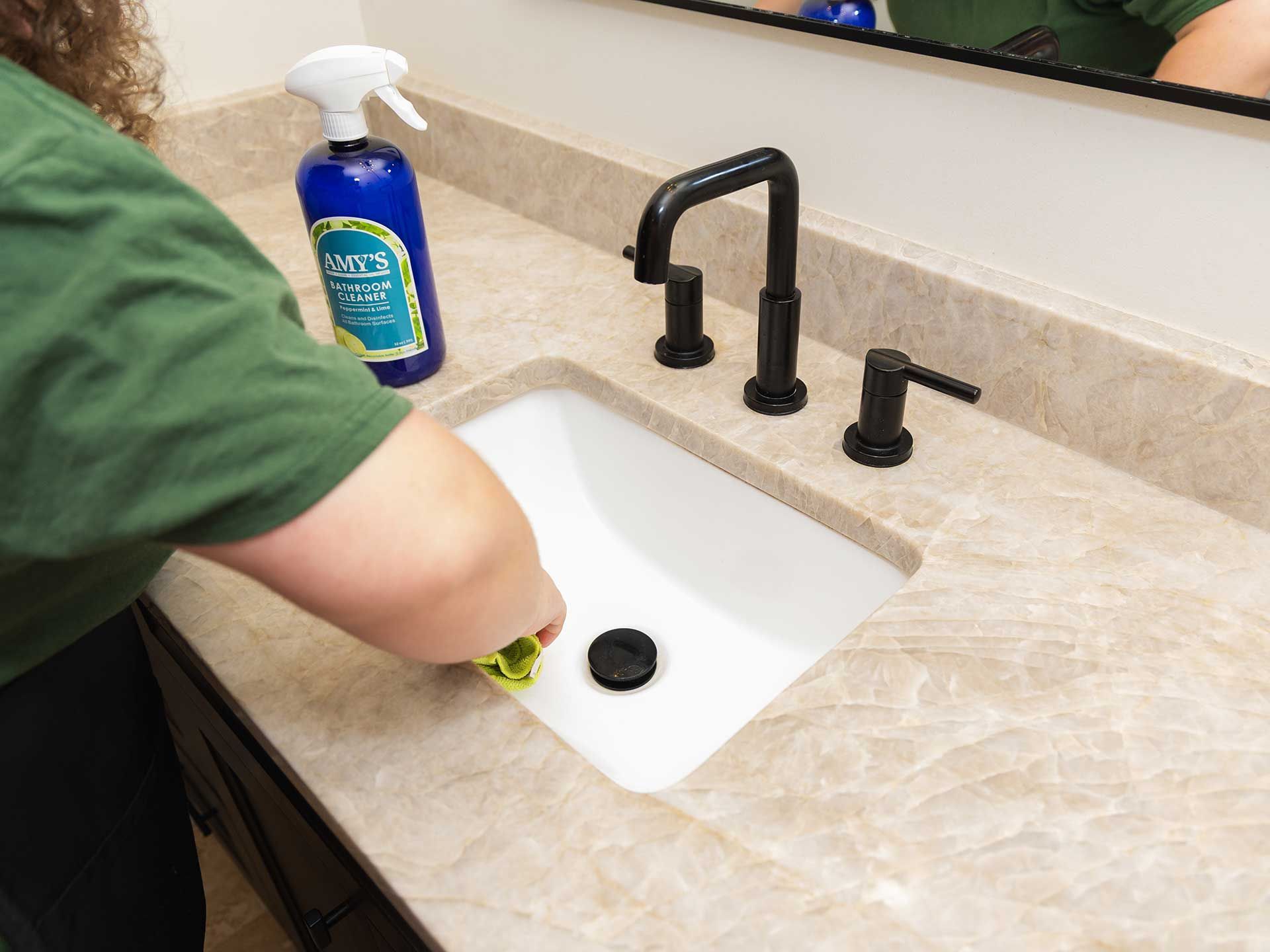 a person cleaning a white bathroom sink with a spray bottle and a cloth