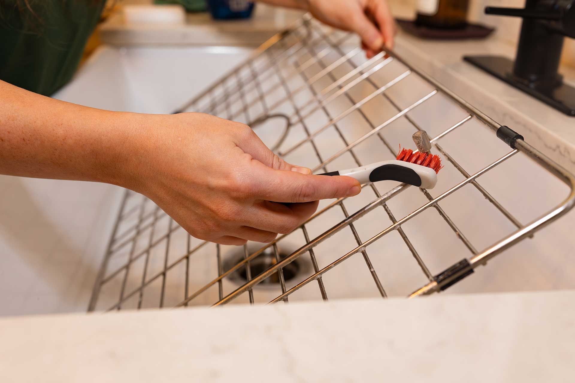 a person cleaning a metal rack in a sink with a brush