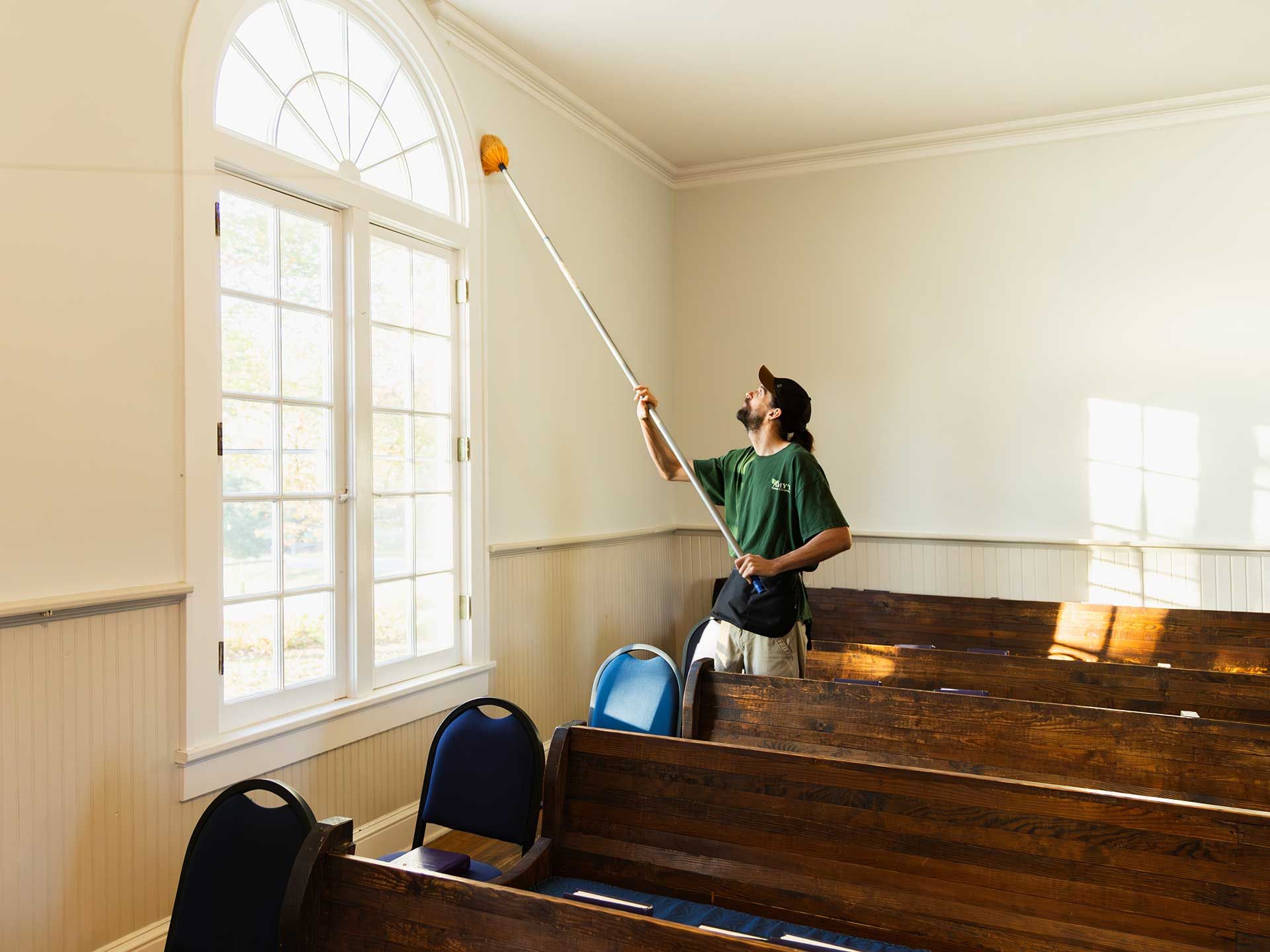 a man cleaning high ceiling in a church with a long-handled tool