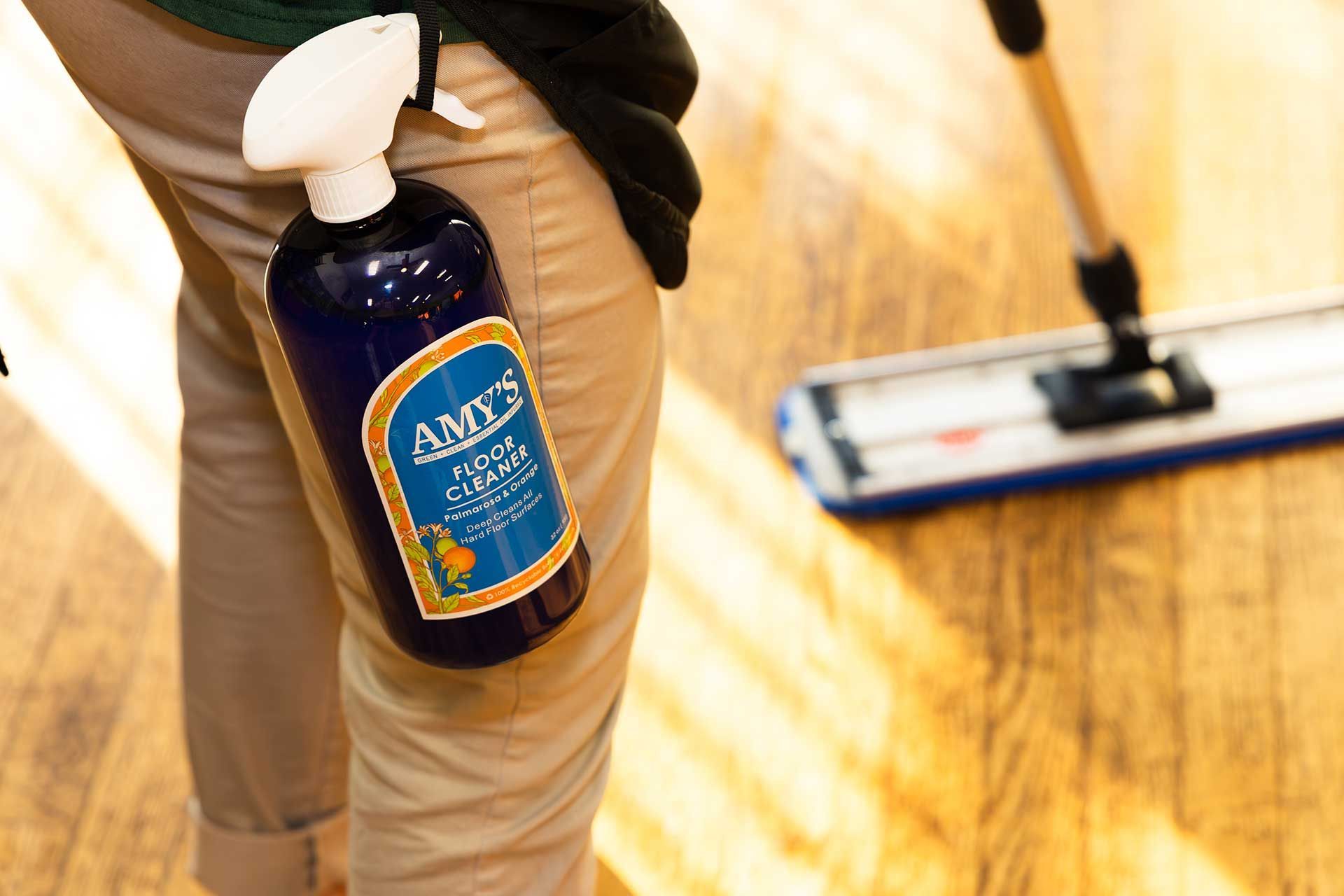 a person with a spray bottle of floor cleaner while mopping a wooden floor