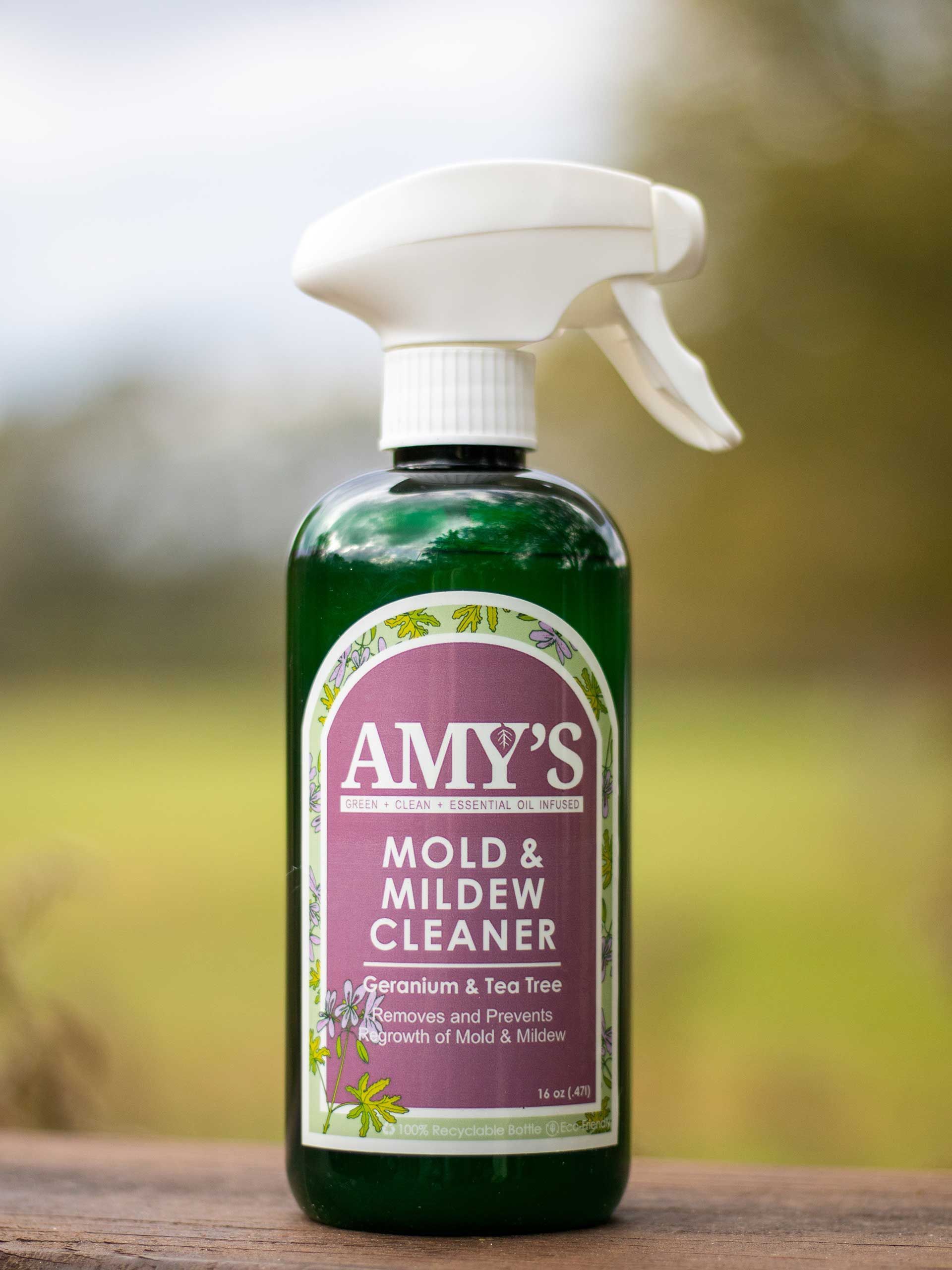 Amy's Mold & Mildew Cleaner bottle with spray nozzle, against a blurred outdoor background