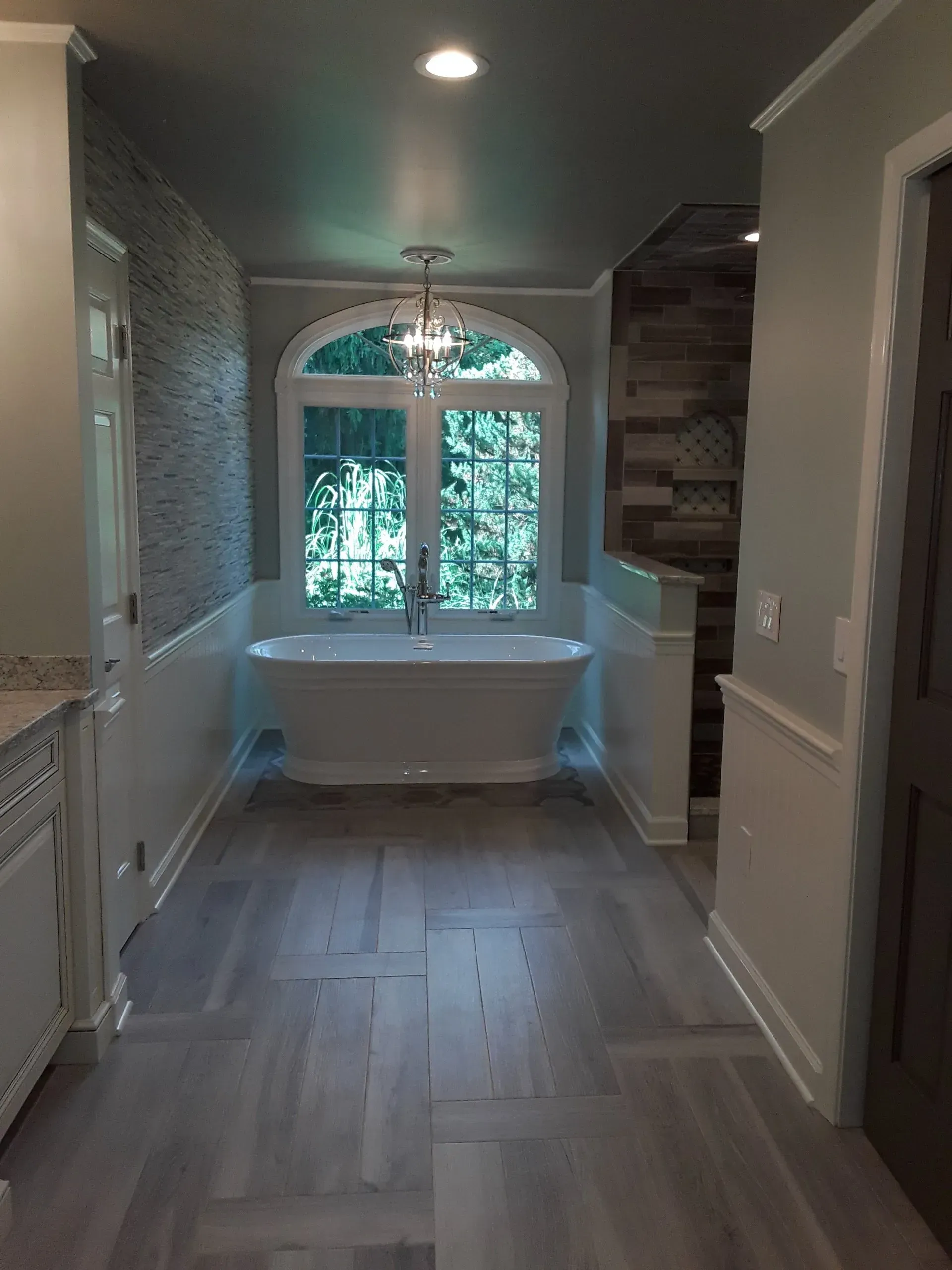 Bathroom with a freestanding tub under an arched window. Gray wood-look flooring and light blue walls.