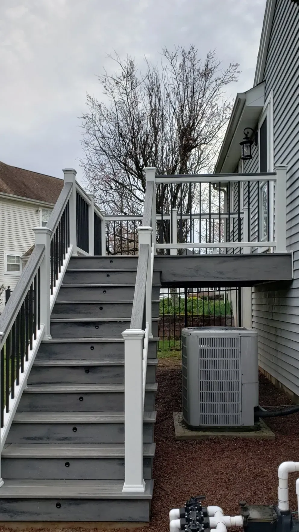 Gray deck and stairs leading up to a white-sided house, with black railing and an AC unit below.