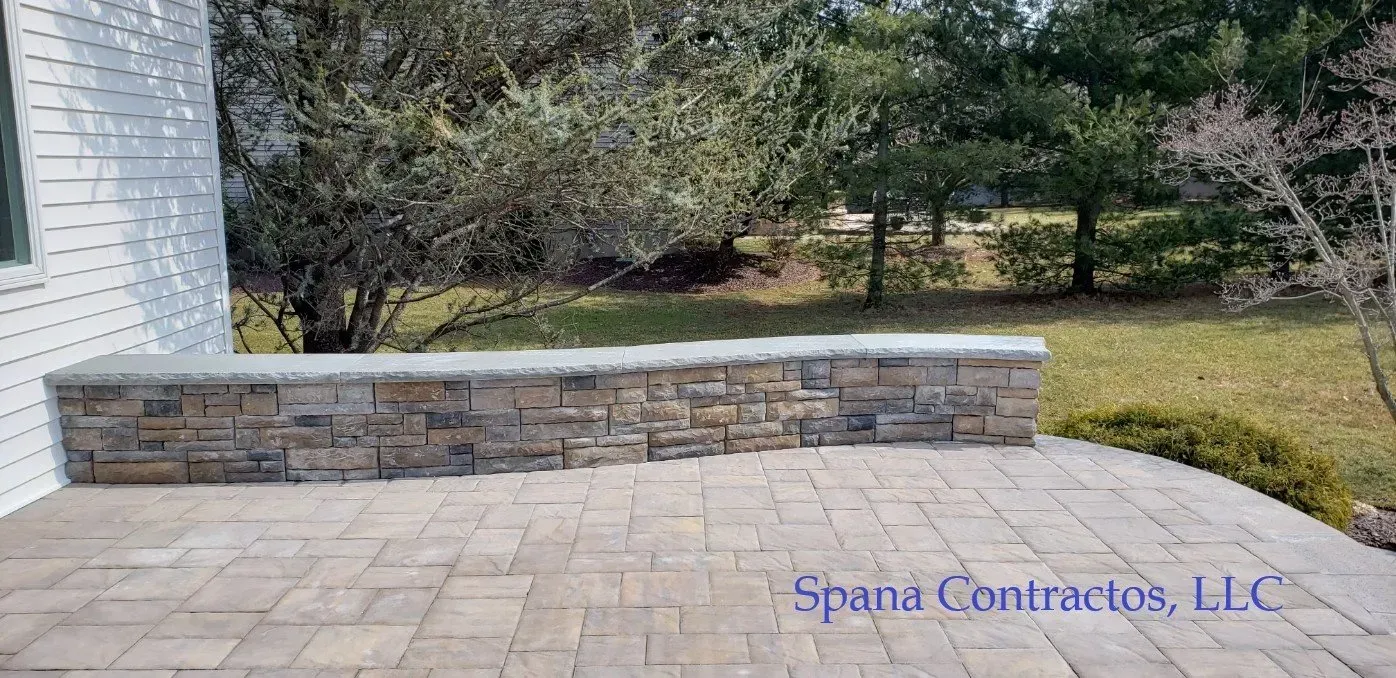 Stone patio with a stone wall and green yard in the background.