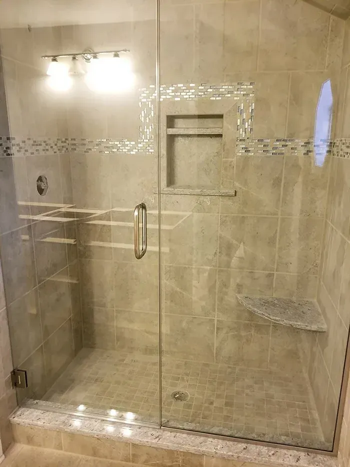 Glass shower with tiled walls, built-in shelves, a corner seat, and a recessed shelf.