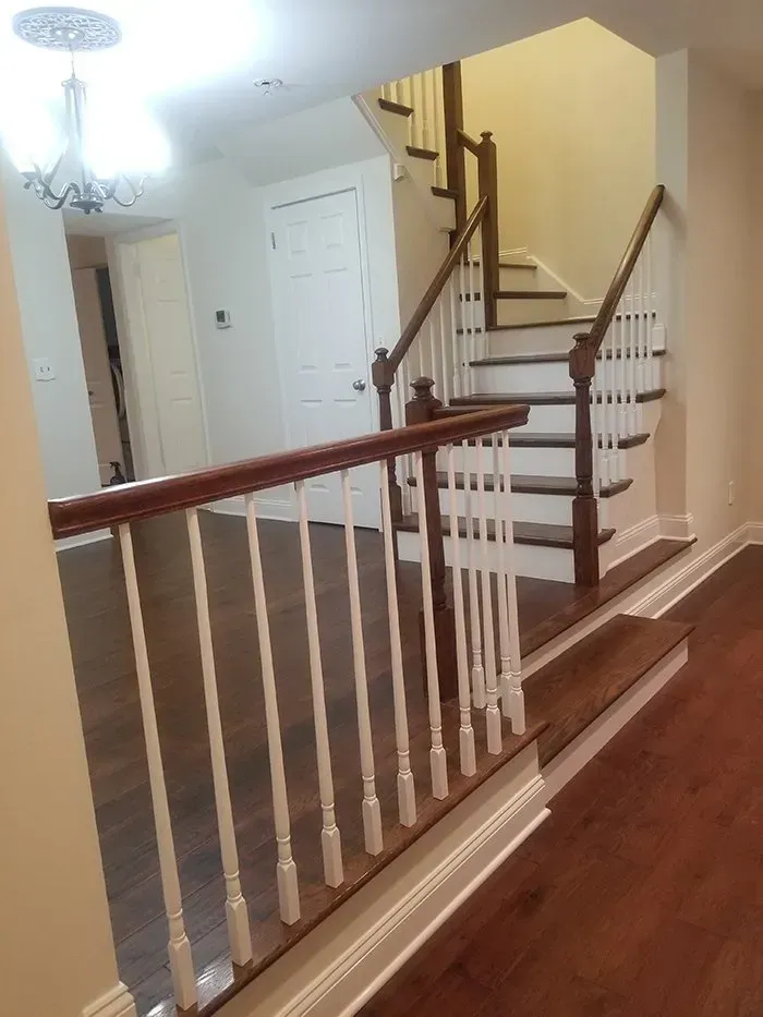 Interior view of a stairwell with white railing, wood stairs, and dark flooring.