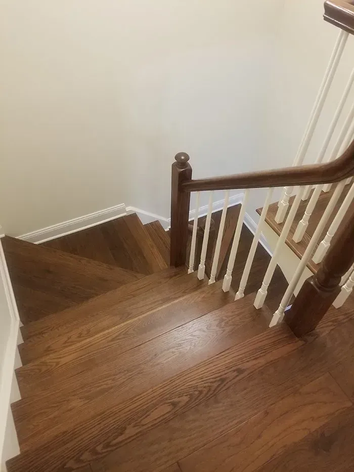 Wooden stairs with a brown handrail and white spindles, viewed from above.