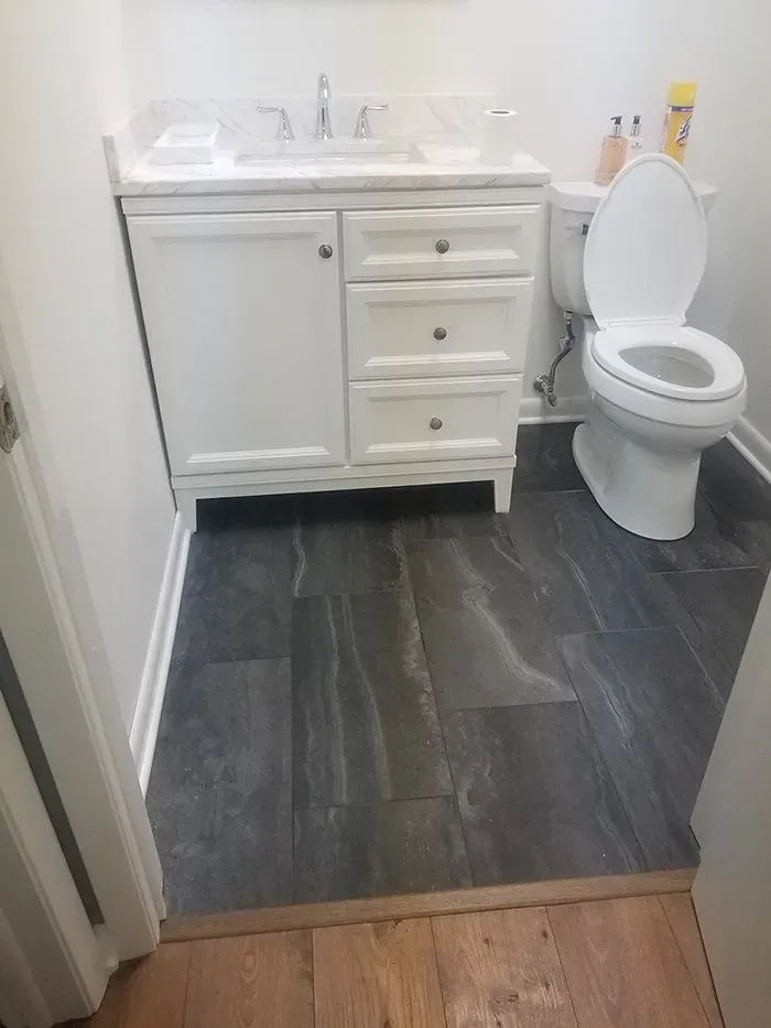 Small bathroom with white vanity, toilet, and dark gray floor tiles.
