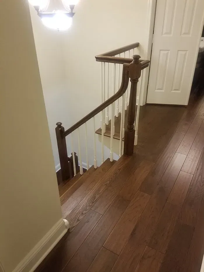 Dark hardwood stairs with wooden railing, leading down from a landing. White wall and door in the background.