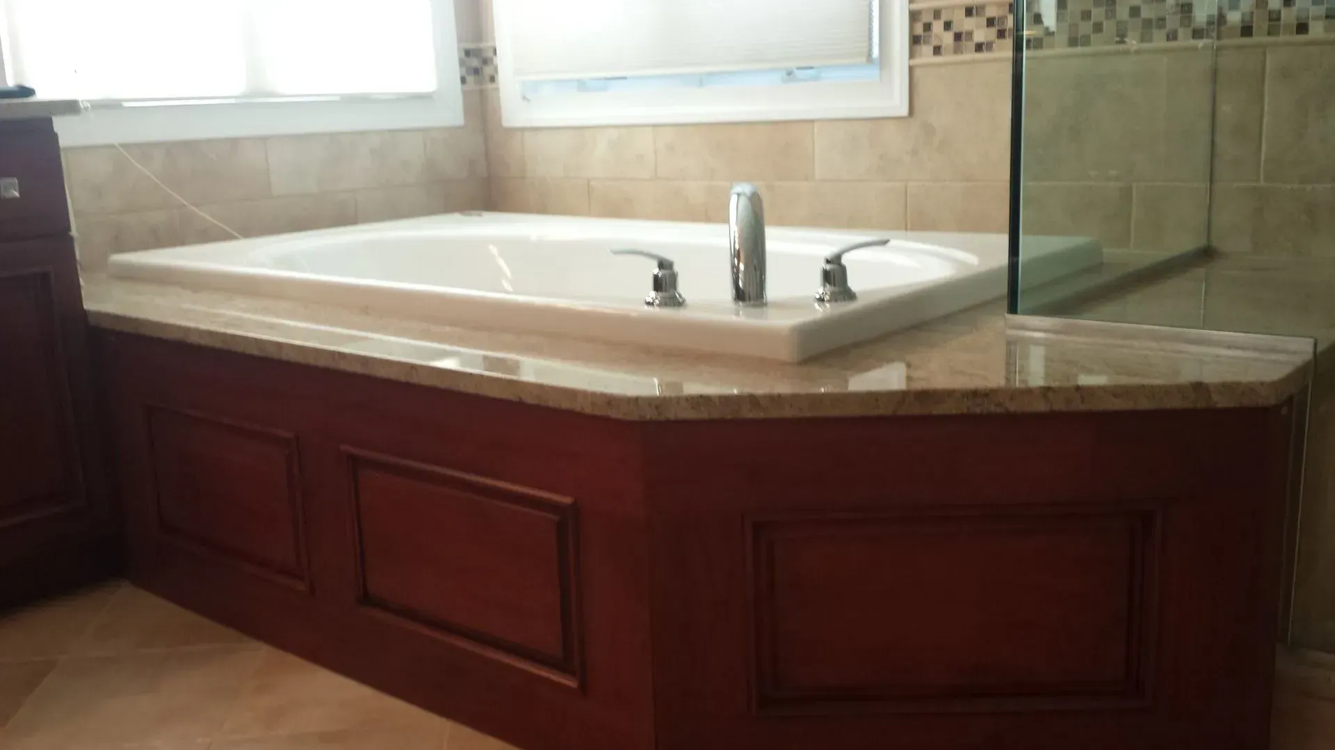 A burgundy-paneled bathtub surround with a cream-colored countertop, a white tub, and a glass shower.