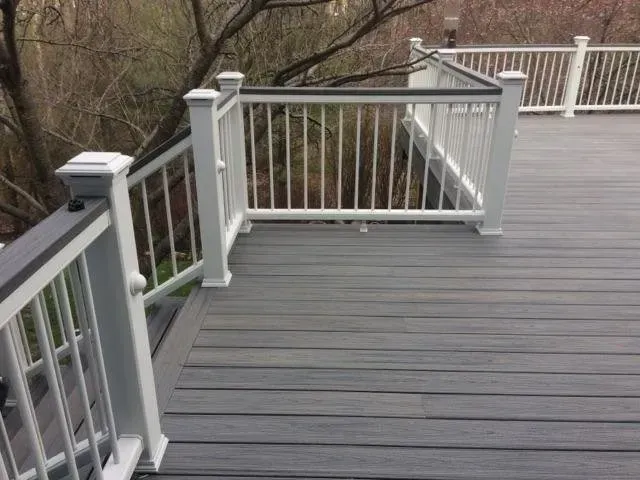 Gray deck with white railing, surrounded by trees.
