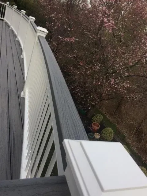 Curving deck with white railing and gray decking, overlooking a blossoming tree.