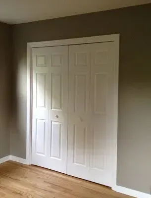 White bi-fold closet doors against gray walls, wood floor in a bedroom.