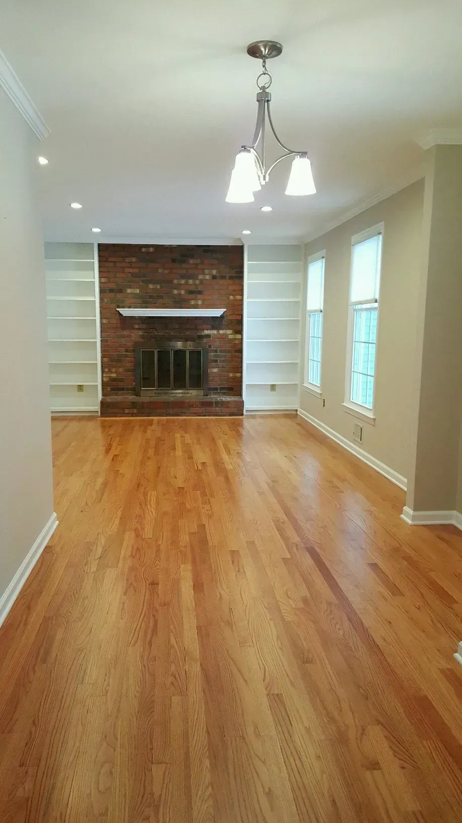 Hardwood floor leads to a brick fireplace flanked by white built-in bookshelves in a living room.