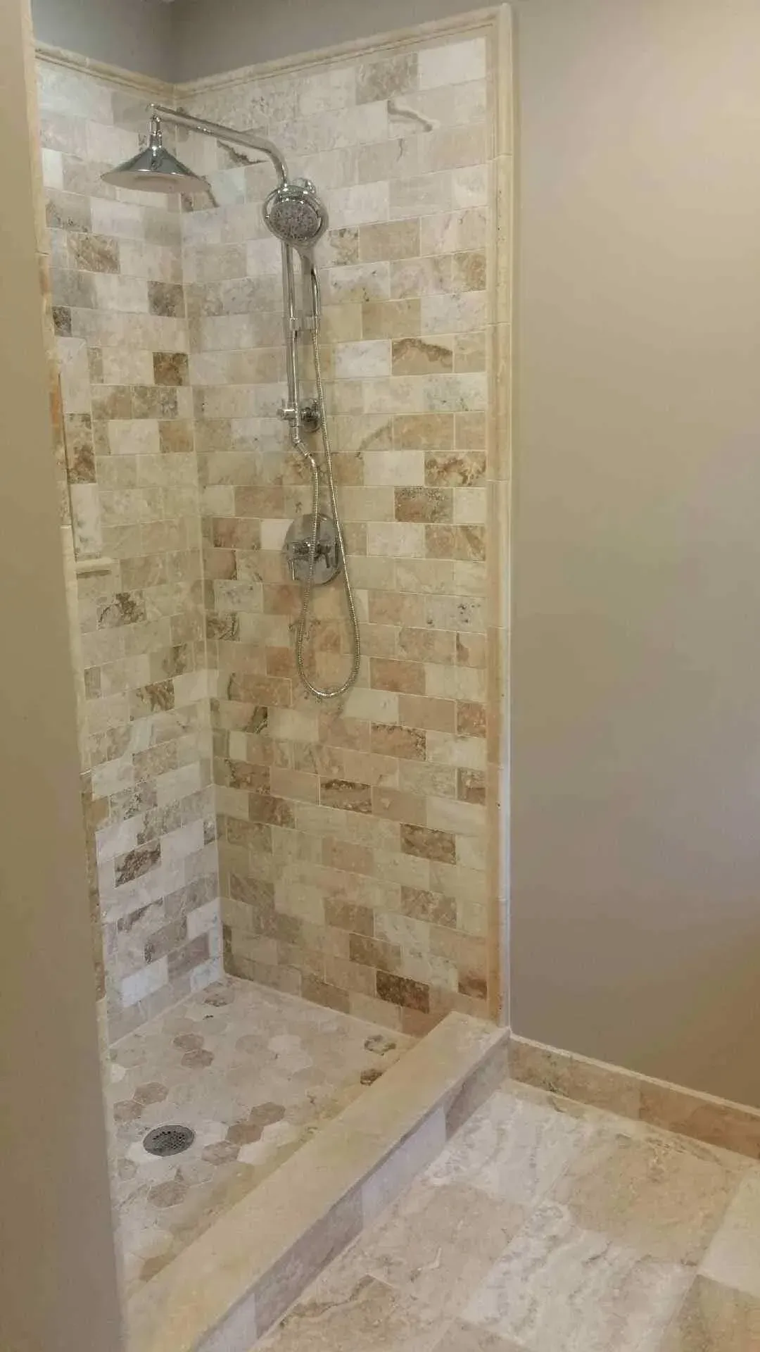 Shower with light-colored stone tile walls and floor, multiple shower heads, and a step-up entrance.