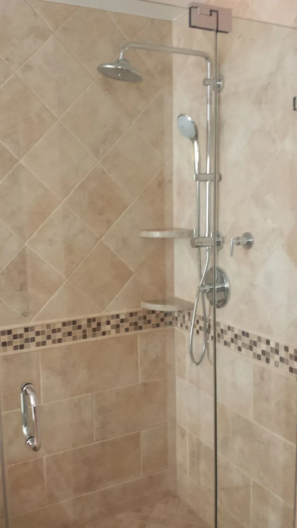 Shower stall with tan tile, glass door, and silver shower fixtures.