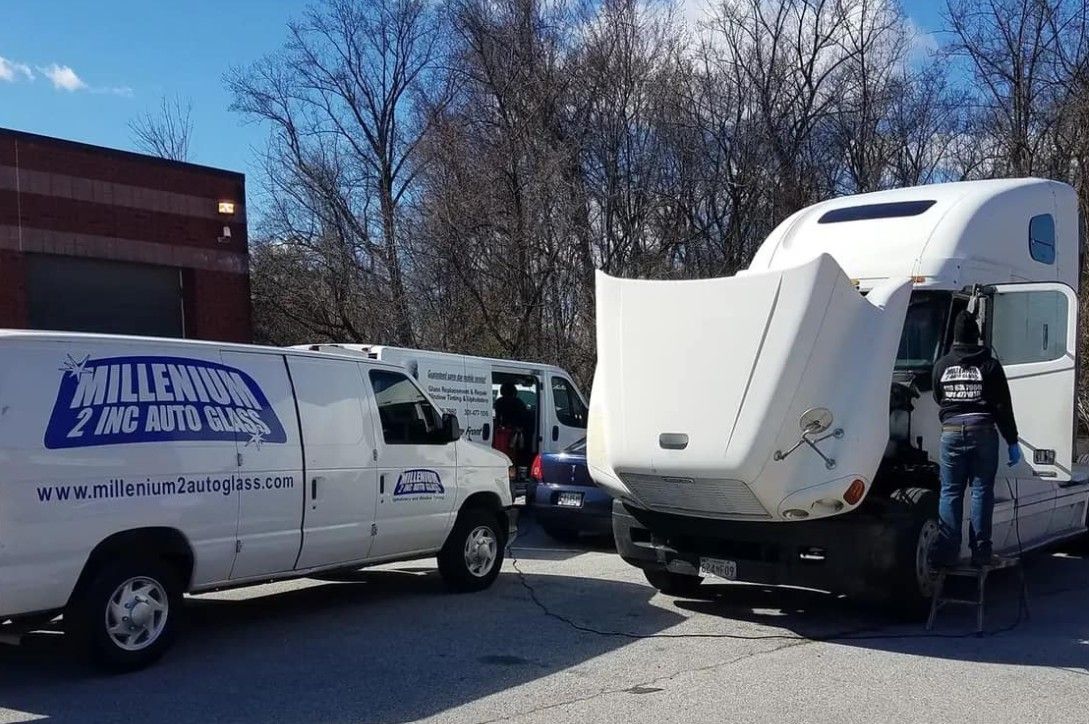 Truck with open hood being worked on by a person next to a white van and a smaller vehicle in a parking area.