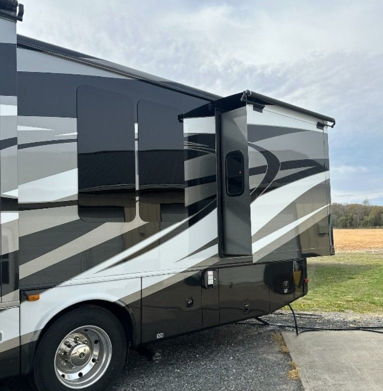 RV with a slide-out extended. It has black, gray, and white paint. The setting is outdoors.