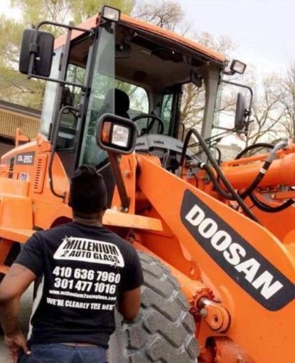 Man in black shirt with logo standing next to orange Doosan construction vehicle.